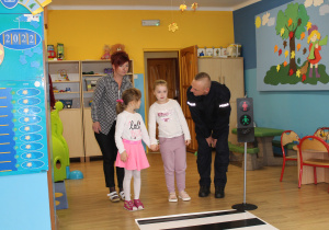 Hana, Maja i pani Ania z funkcjonariuszem Policji podczas ćwiczeń przechodzenia przez jezdnię (ćwiczenia w sali)